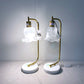 Pair of table lamps with gold arms and white lampshades on a gray surface.