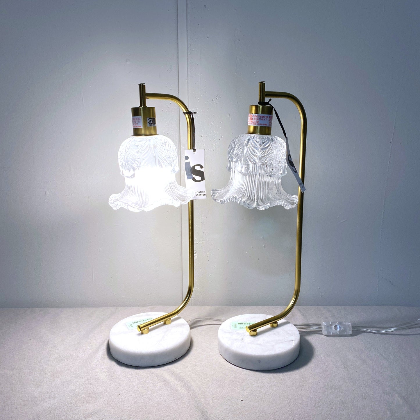 Pair of table lamps with gold arms and white lampshades on a gray surface.