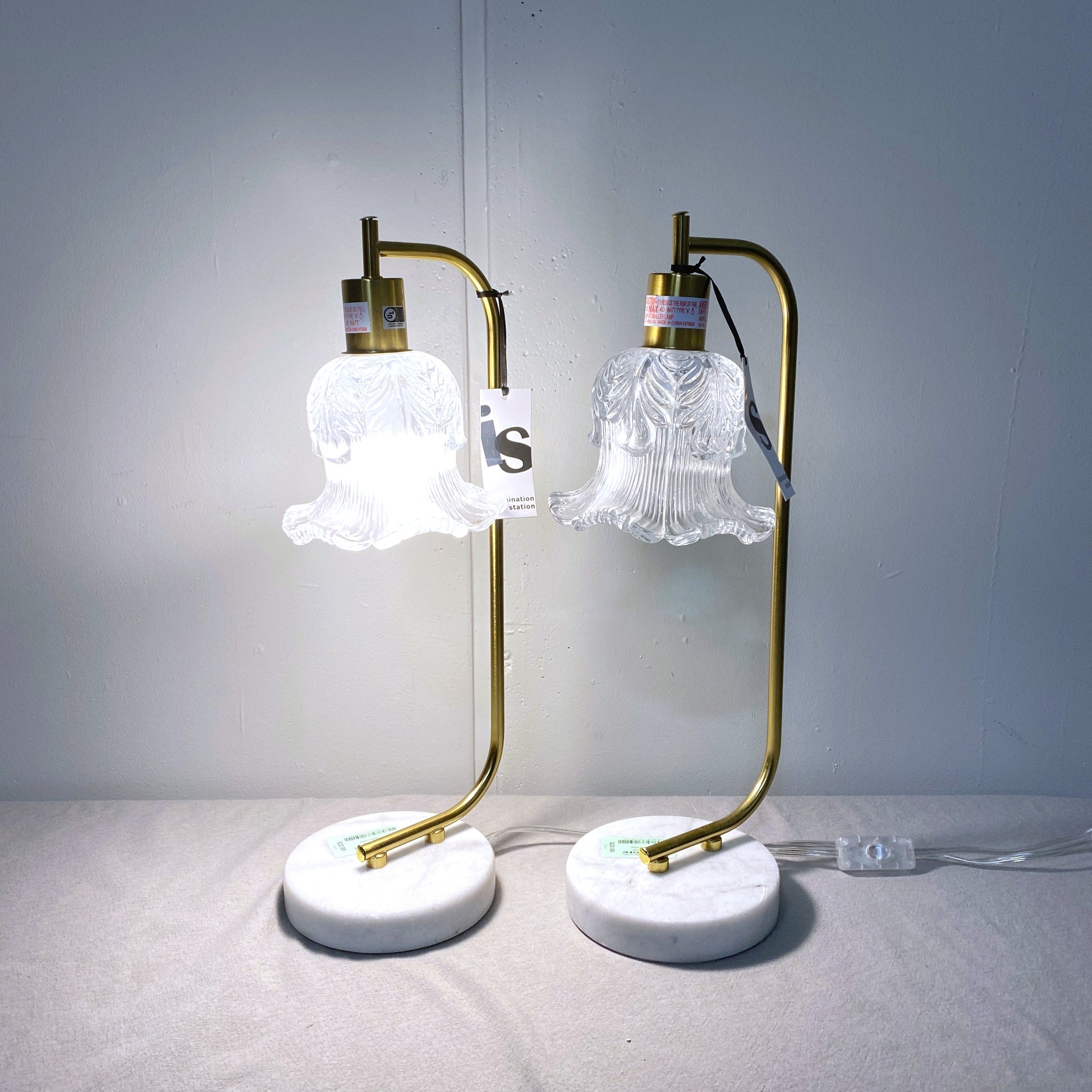 Pair of table lamps with gold arms and white lampshades on a gray surface.