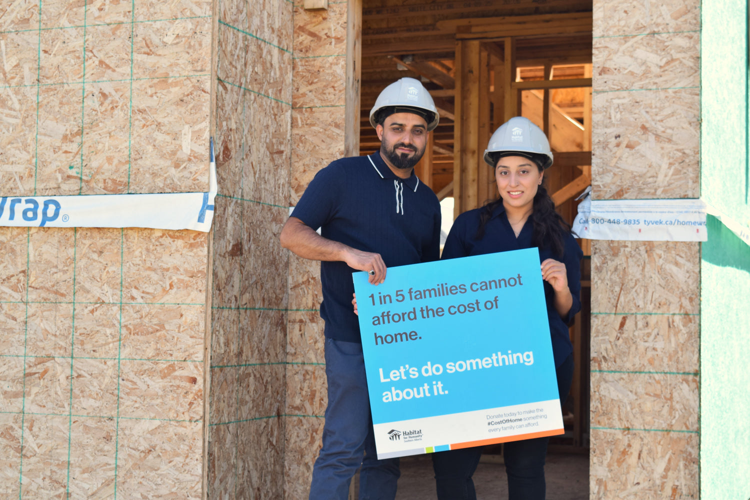 Habitat homeowners hold a blue sign that states "1 in 5 families cannot afford the cost of home. Let's do something about it." 